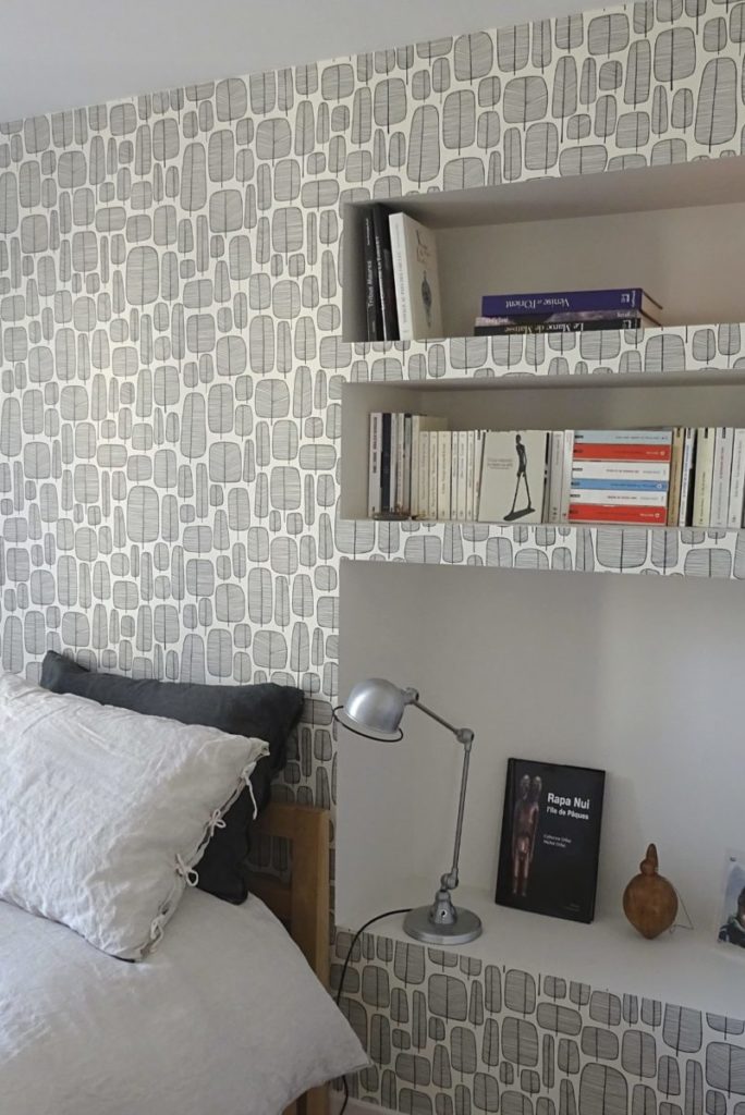 photo de détail de decoration interieure sur une niche transformée en table de chevet avec une lampe de chevet et un papier peint moderne geometrique derrière la tête de lit
