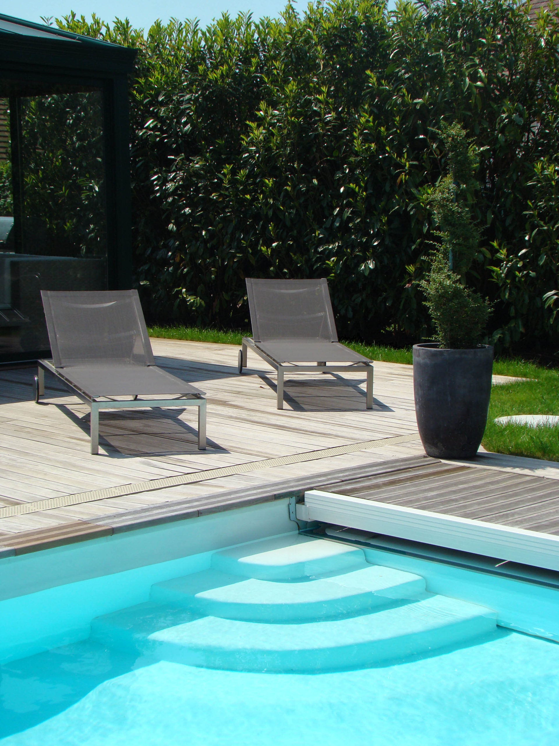 vue de l'entrée de la piscine avec des escaliers blanc en beton et sur la terrasse deux chaises longues